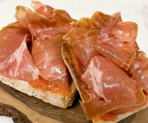Toasted bread with reddish spread and thinly sliced cured ham.