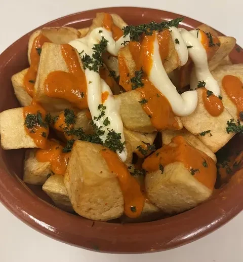 Patatas Bravas with red and white sauces and green herbs.
