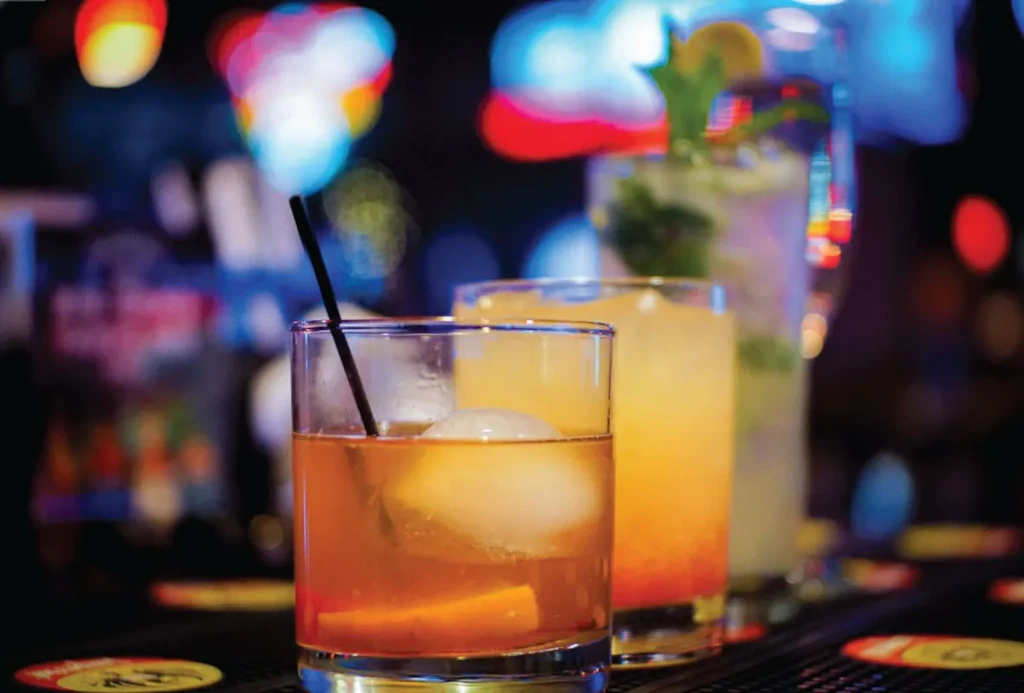 Three diverse cocktails on a bar counter with a vibrant, blurred background.
