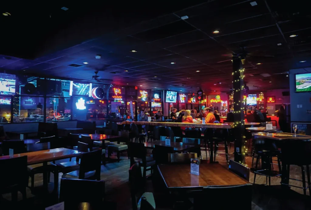 Energetic sports bar interior at night, filled with screens and neon lights.