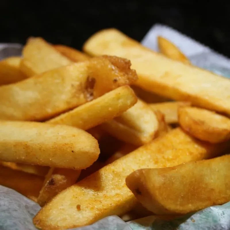 Close-up of golden-brown, thick-cut, seasoned french fries in a basket.