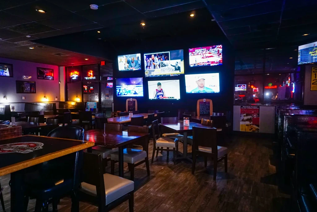 Dimly lit sports bar interior with a wall of screens showing sports.