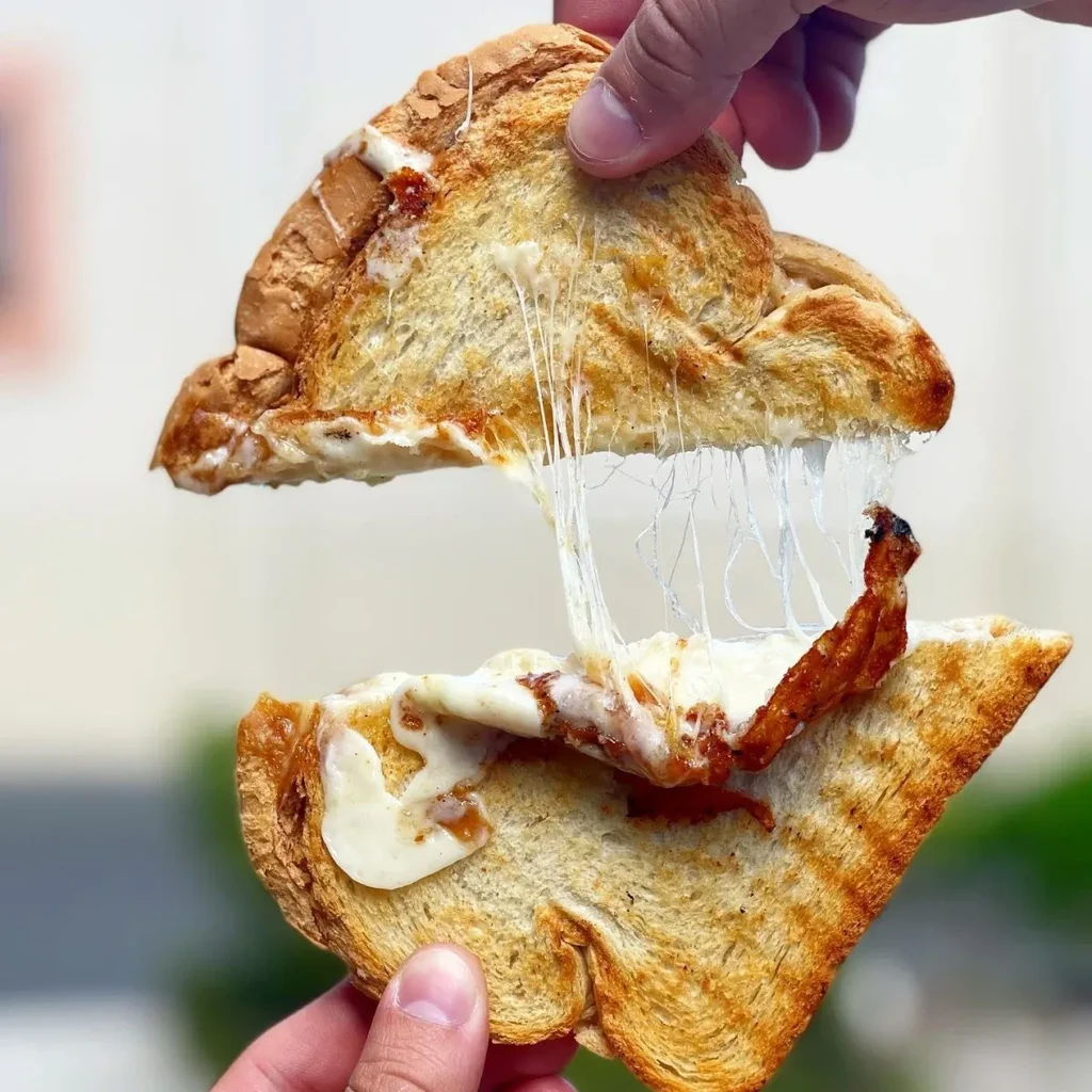 Hands pull apart a golden-brown grilled cheese with a cheese pull.