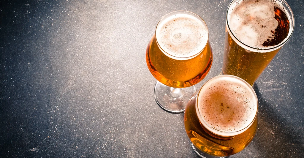 Three glasses of amber beer with foam on a dark, textured surface.