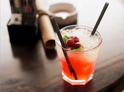 Red-orange cocktail with crushed ice, berries, mint, and two straws.