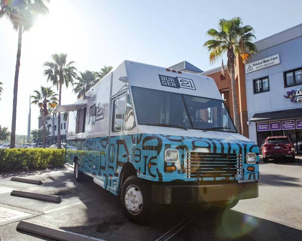 Burger 21 food truck in a sunny commercial lot with palm trees.