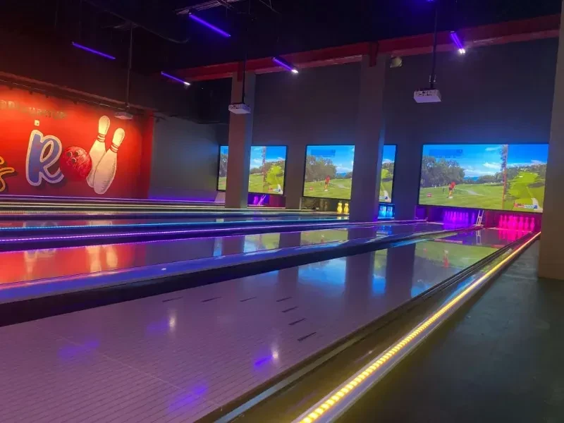 Modern bowling alley with neon-lit lanes and golf simulation screens.