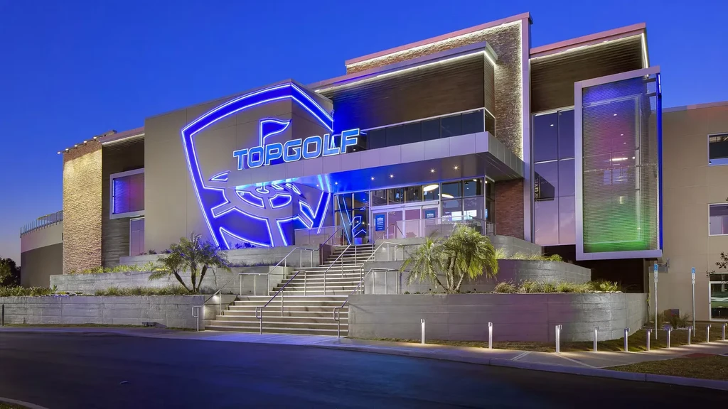 Large modern Topgolf building at dusk with a bright blue neon logo.