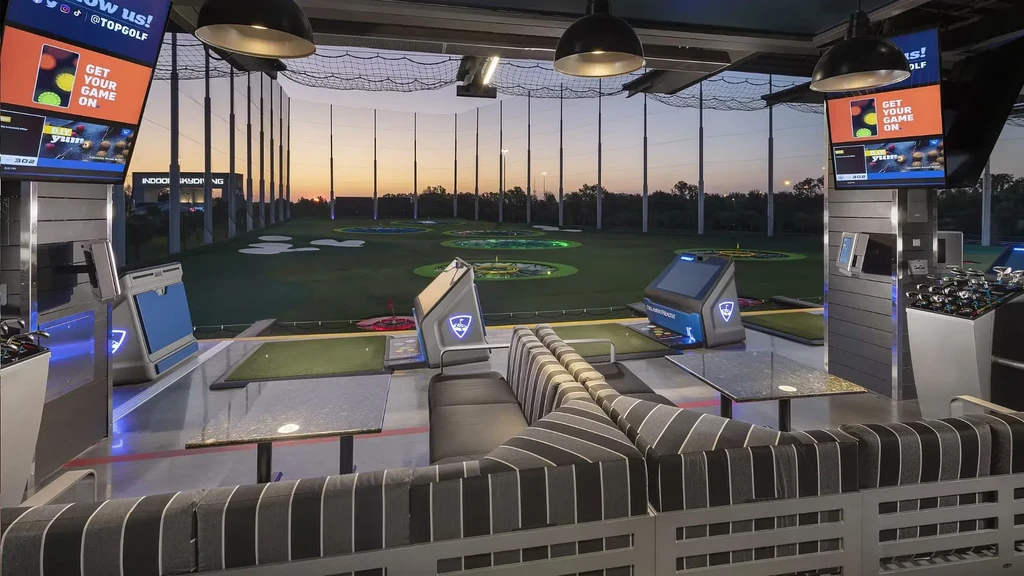 Inside Topgolf bay at dusk, illuminated range targets and digital screens.