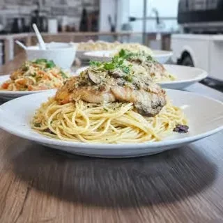 A plate of pasta with pan-seared fish, herbs, and sauce.