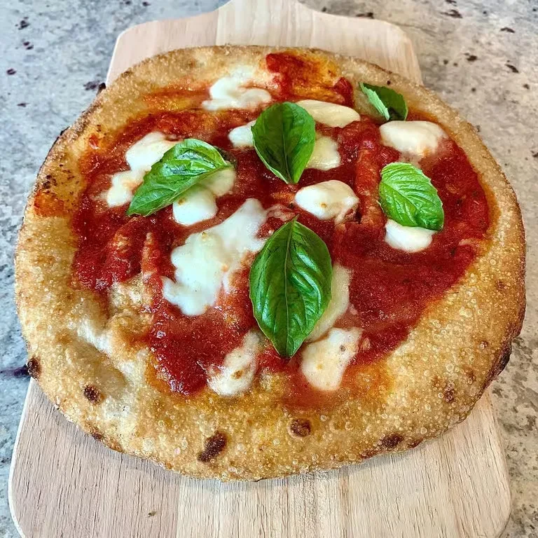 Overhead Neapolitan pizza with charred crust, tomato, mozzarella, basil.
