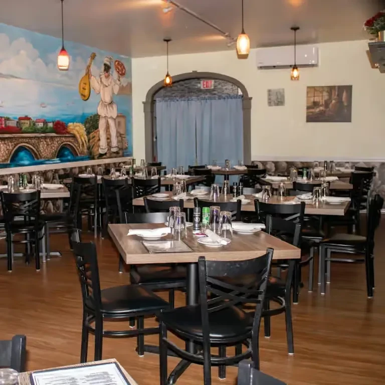 Dining area with wooden tables, black chairs, and a waterside town mural.