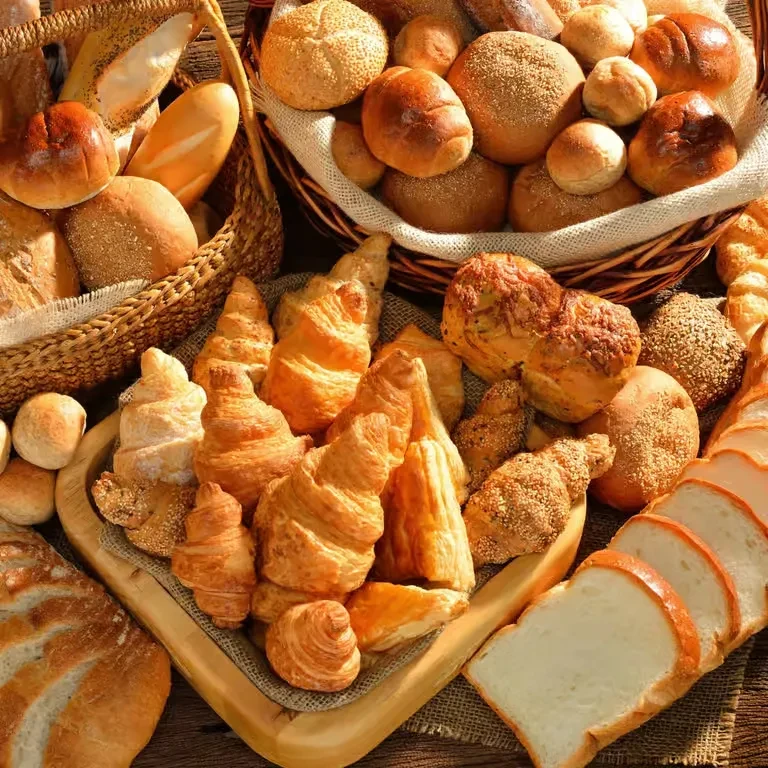 Assortment of freshly baked bread rolls, croissants, pastries, and sliced white bread.