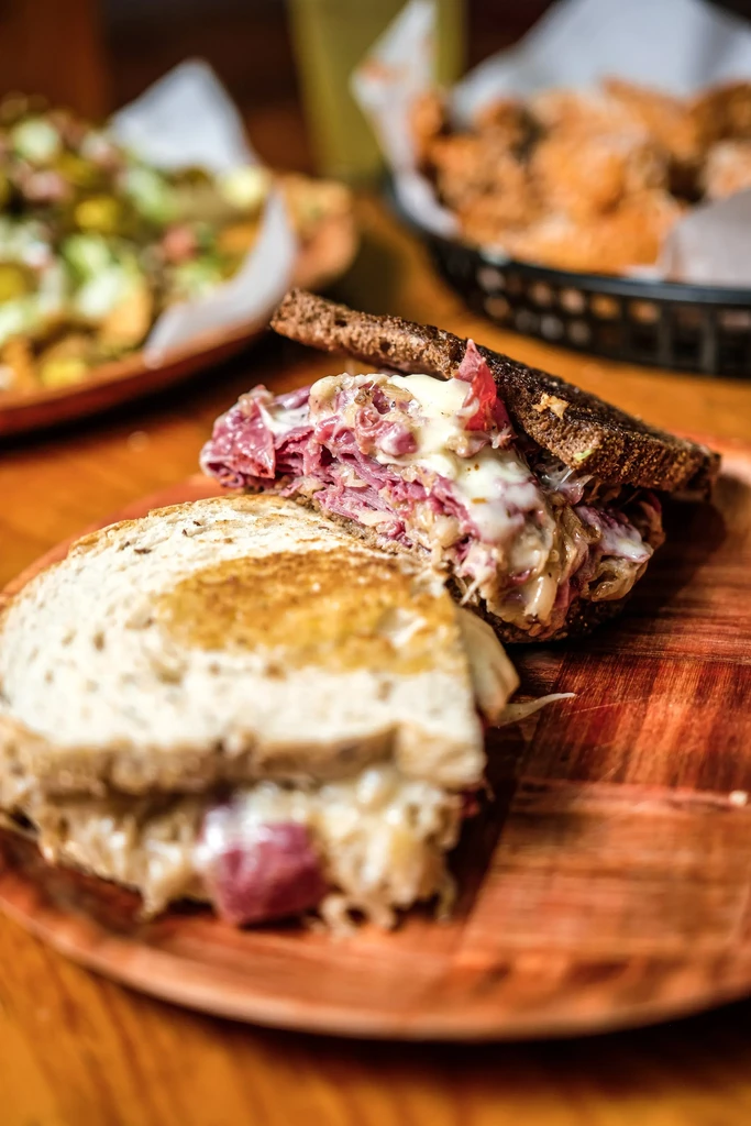 Close-up Reuben sandwich cut in half on a rustic wooden plate.