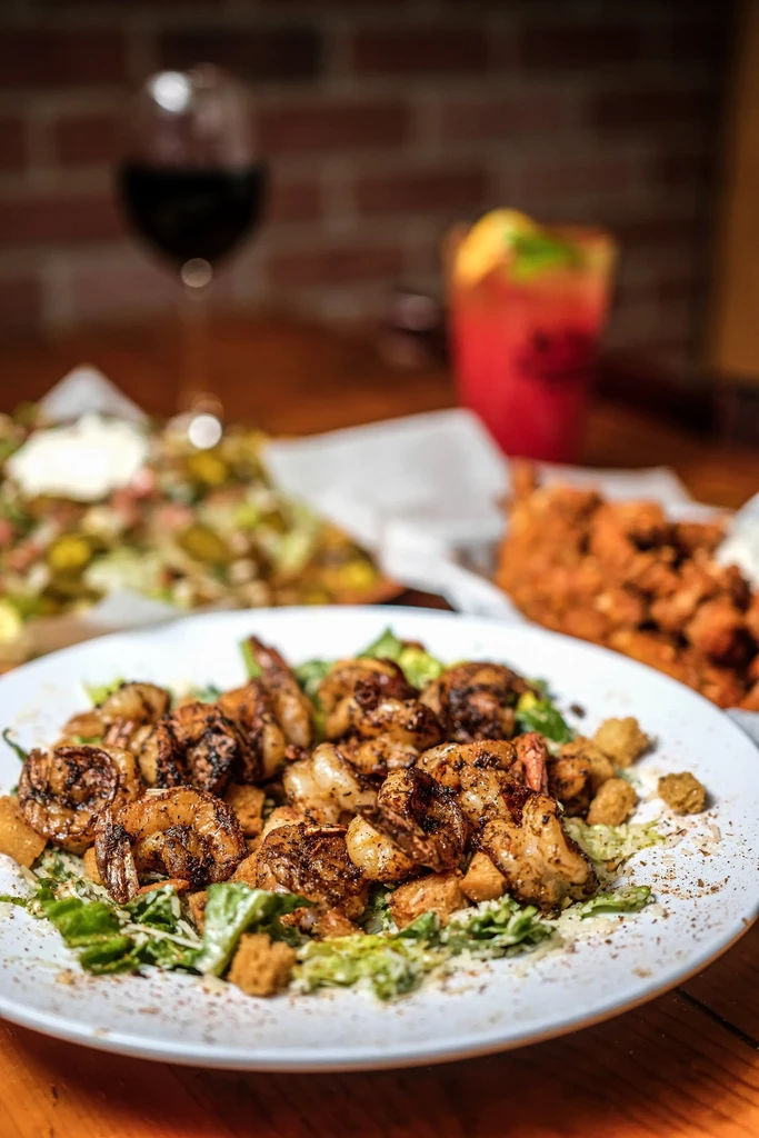 Grilled shrimp salad with lettuce and croutons on a wooden table.