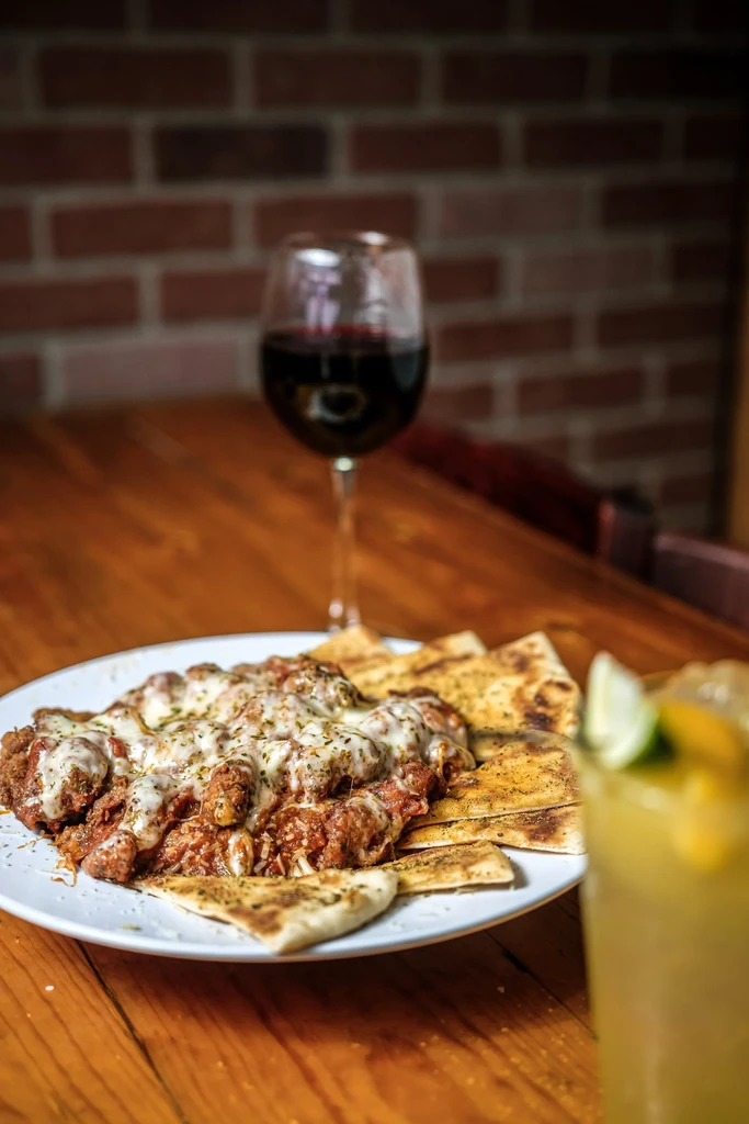 Close-up: Cheesy meat dish, flatbread, red wine, and a garnished cocktail.