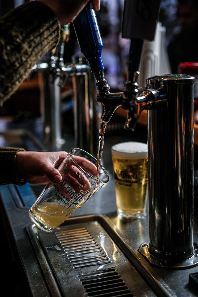 Hand pouring beer from a tap into a glass at McDivots Sports Bar.