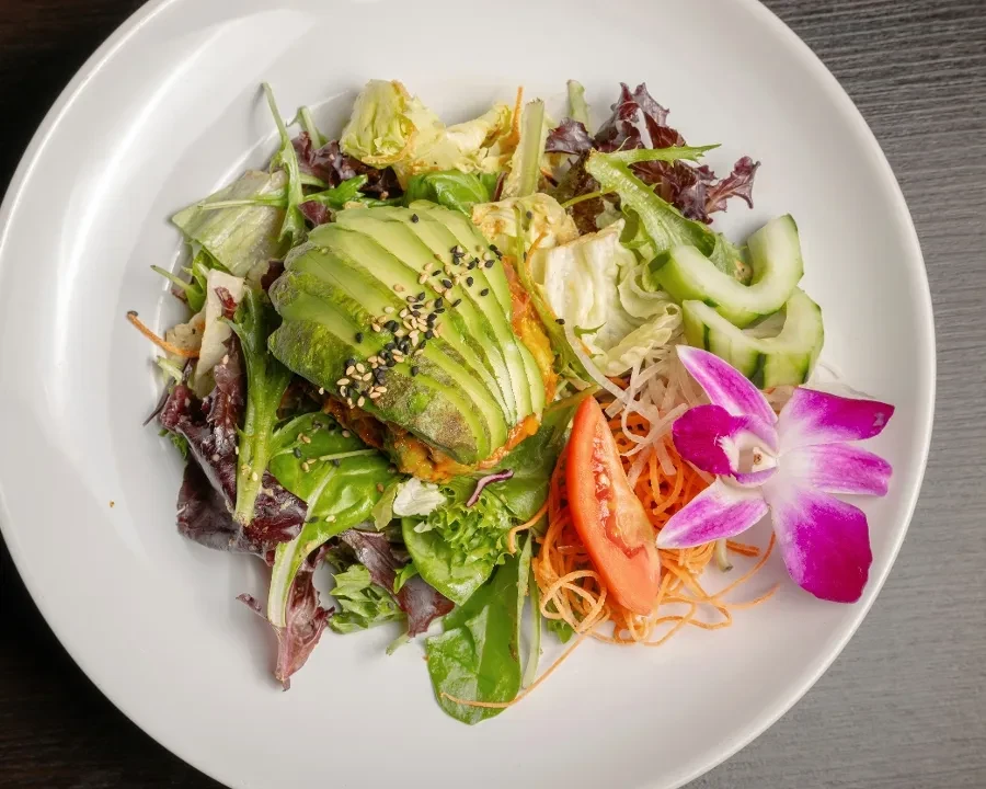 Arranged salad with fanned avocado, sesame, various vegetables, and orchid.