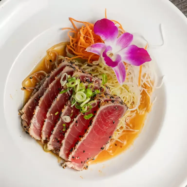 Seared sesame tuna on noodles with vegetables and an orchid.