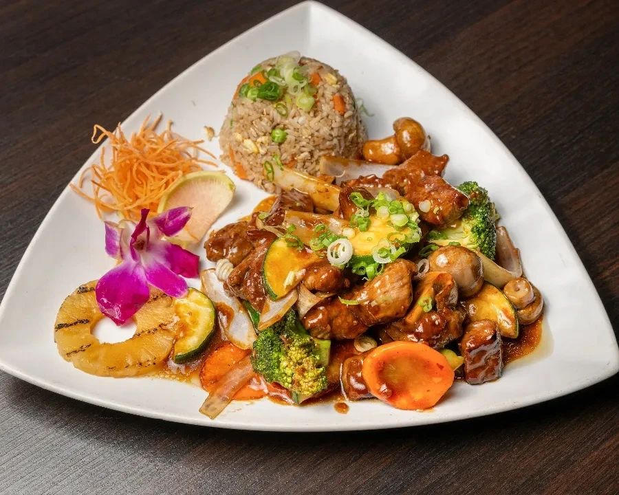 Plated Asian stir-fry with fried rice, sauced meat, colorful vegetables, orchid.