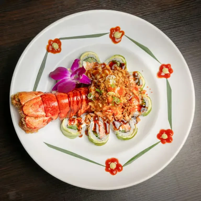 Plated sushi rolls, lobster tail, crispy toppings, and purple orchid.