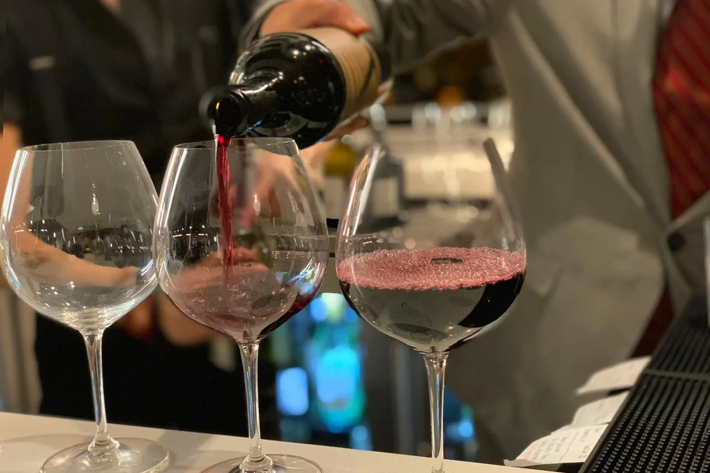 Server pours red wine into a glass in an upscale setting.