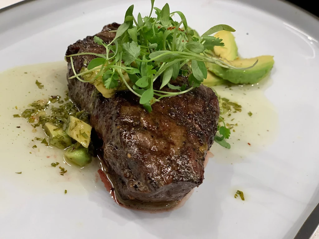 Meticulously plated seared steak with microgreens, avocado, and green salsa.