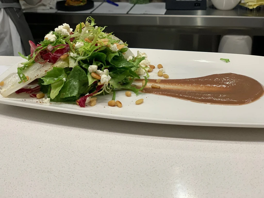 Mixed green salad with white cheese, pine nuts, brown dressing.