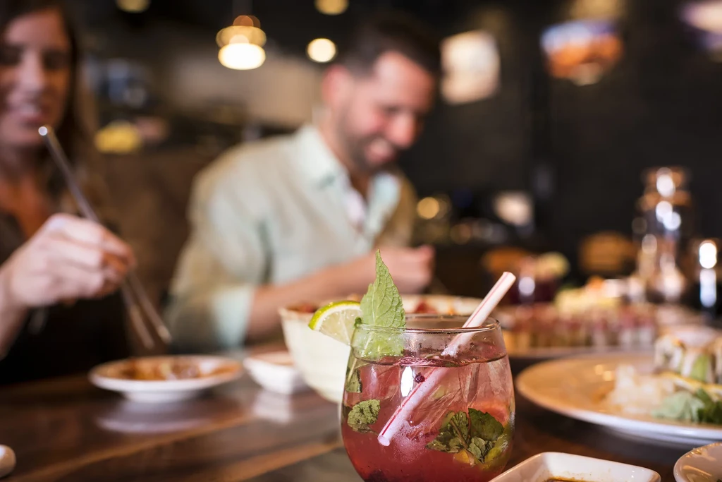 Red drink garnished with mint and lime on a table with sushi.