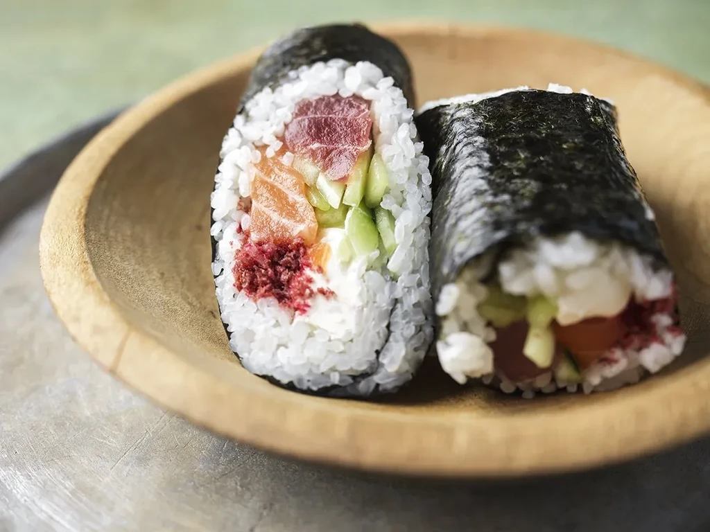Two sushi hand rolls with tuna, salmon, cucumber, and rice on wood.