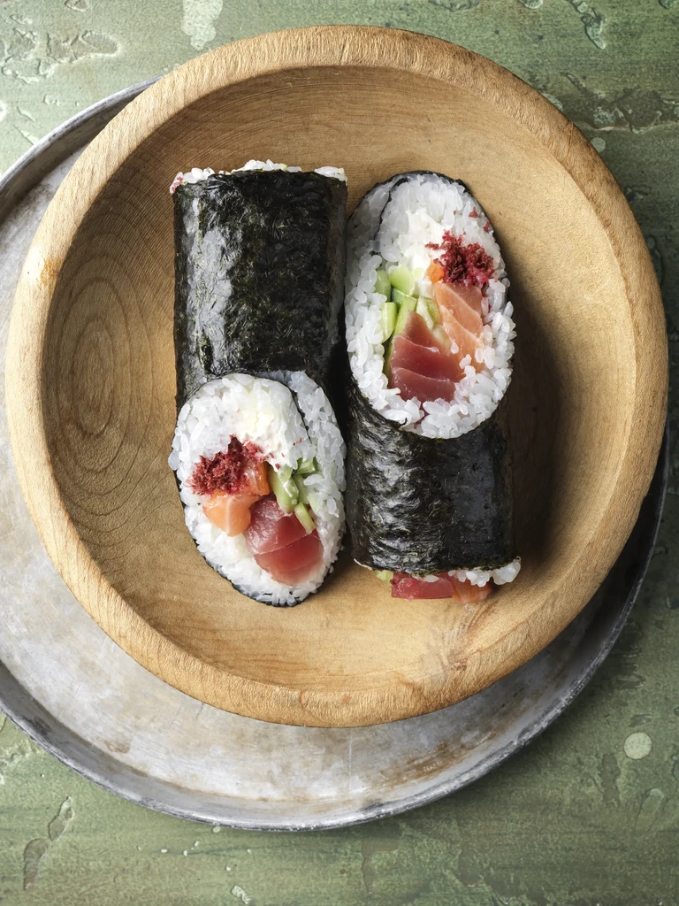 Four sushi rolls with salmon, tuna, cucumber, in a wooden bowl.