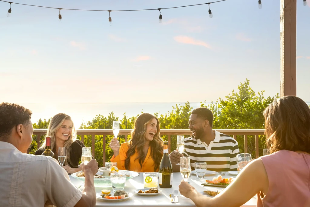 Group dines outdoors with oysters, wine, and a scenic water view.