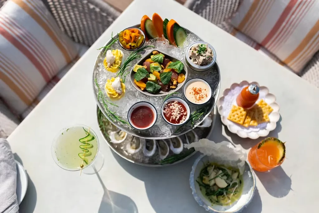 Overhead view of a vibrant two-tiered seafood platter and cocktails outdoors.
