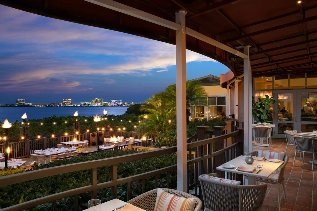 Lush terraced restaurant at dusk, string lights, fire pit, city view.