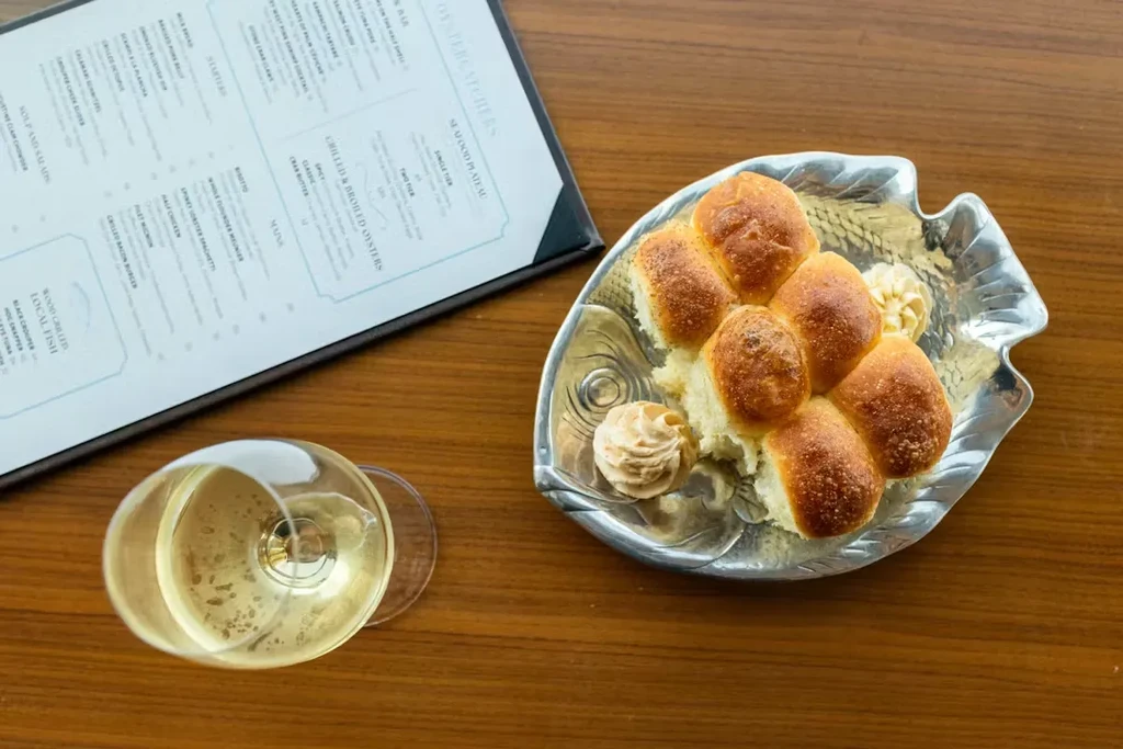 Restaurant table with dinner rolls on a fish platter, wine, and menu.