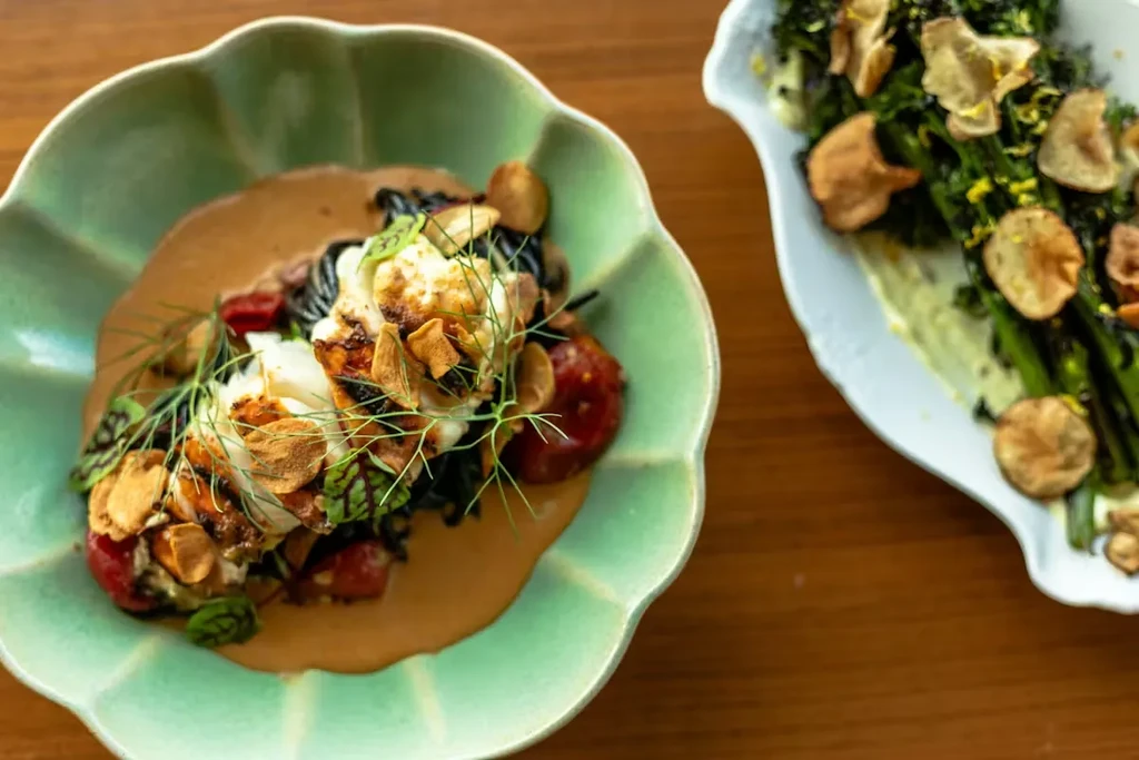 Close-up of seared fish with garlic and a broccoli dish on wood.