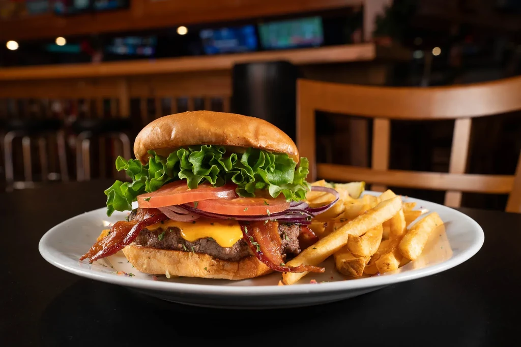 Close-up of a stacked burger and fries on a plate, restaurant setting.
