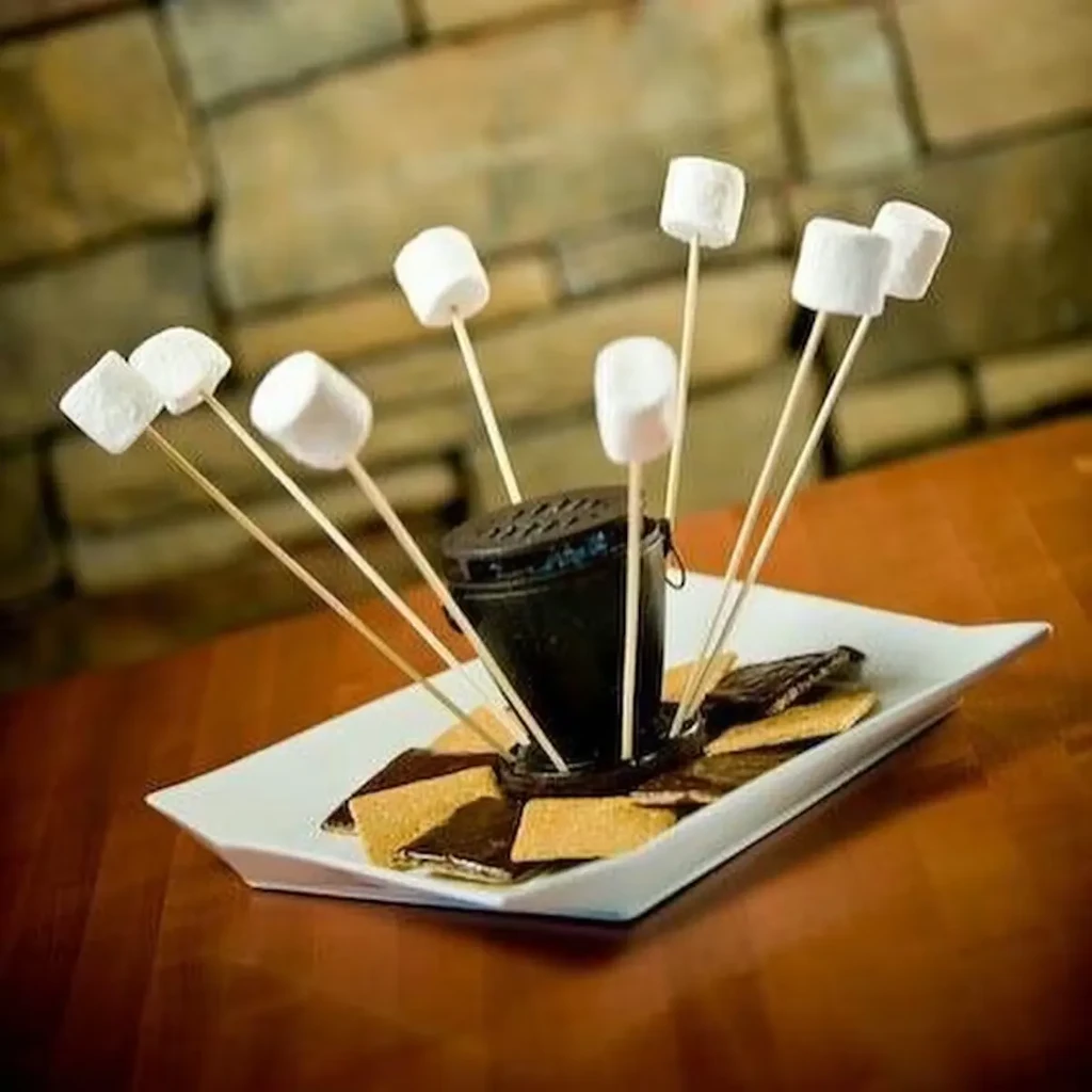 S'mores setup with marshmallows, crackers, and chocolate around a heating pot.