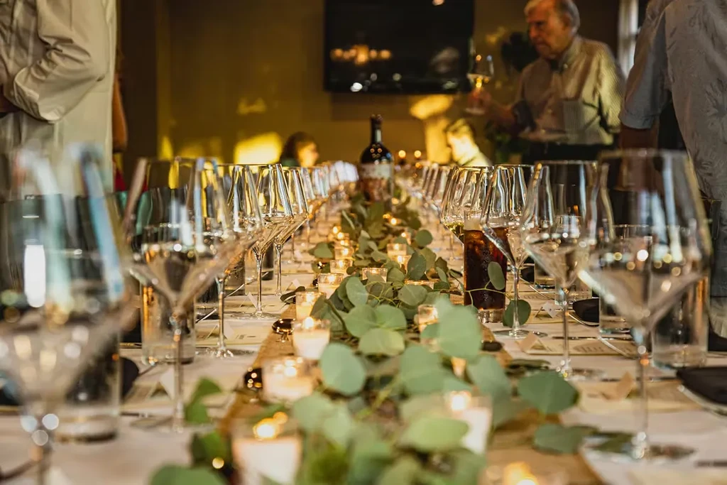 Elegant dining table set with rows of wine glasses, candles, and foliage.