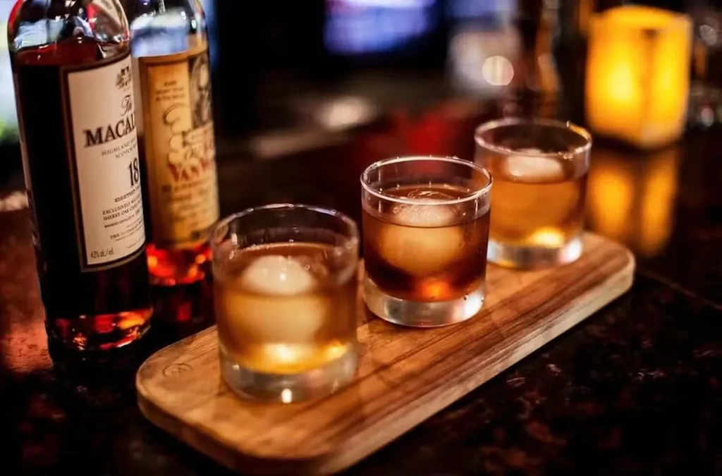 Three whiskey glasses with spherical ice, Macallan 18 bottles on wooden board.
