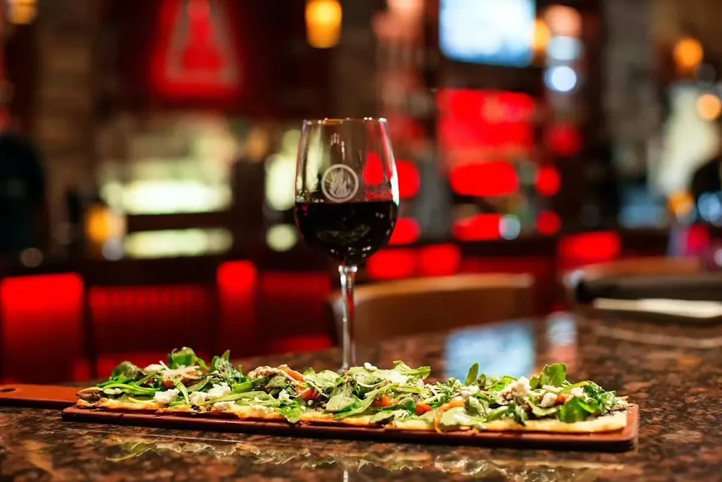 Flatbread with arugula and cheese, red wine, restaurant setting.