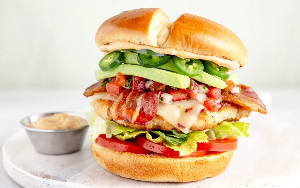 Stacked chicken sandwich with bacon, avocado, pico de gallo, and jalapeño slices.