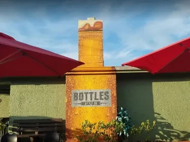 Bottles Pub exterior with beer glass-shaped chimney and red umbrellas.
