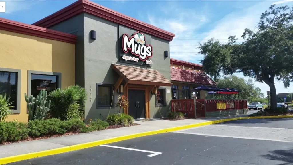 Colorful Mugs Sports Bar & Grill exterior with patio and clinking beer mugs logo.
