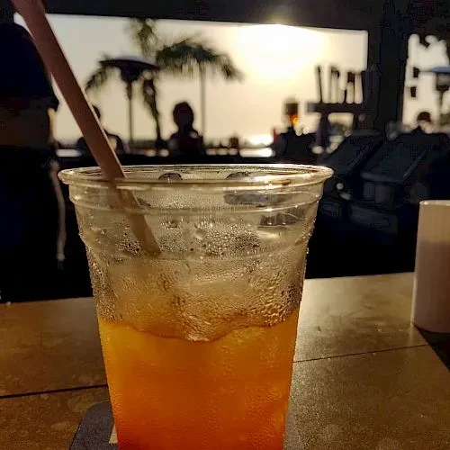 Iced orange drink in a plastic cup, silhouetted sunset background.