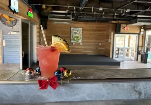 Red-pink cocktail, fruit, straw, Christmas ornaments on a bar counter.
