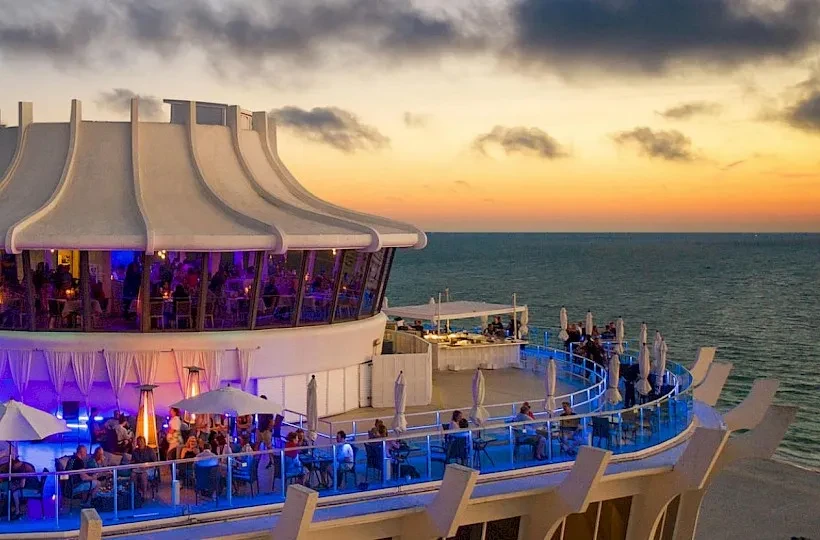 Modern multi-level oceanfront restaurant with dome and terraces at sunset.