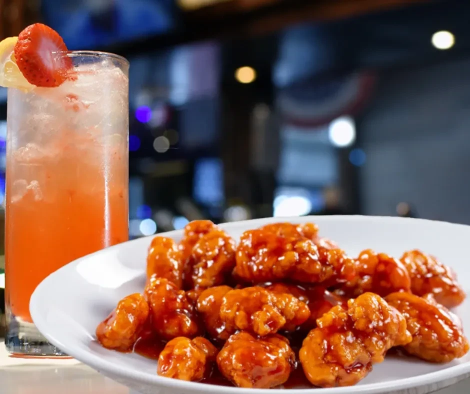 Effervescent orange drink and sauced chicken wings in a restaurant.
