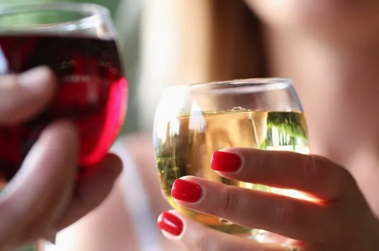 Close-up: Two hands toast stemless glasses with red and golden drinks.