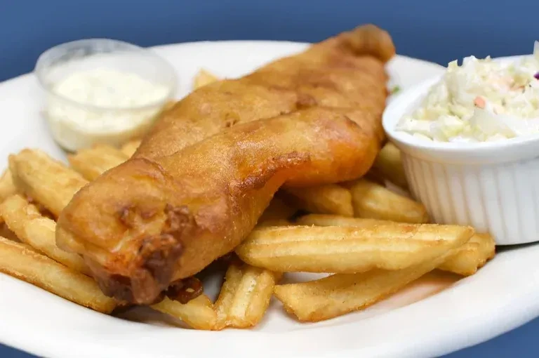 Plate of golden fish and chips with tartar sauce and coleslaw.